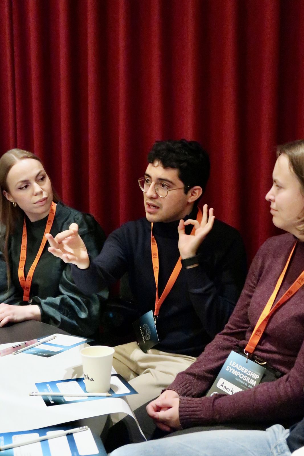 Three participants in orange lanyards deep in conversation at The VALE Symposium