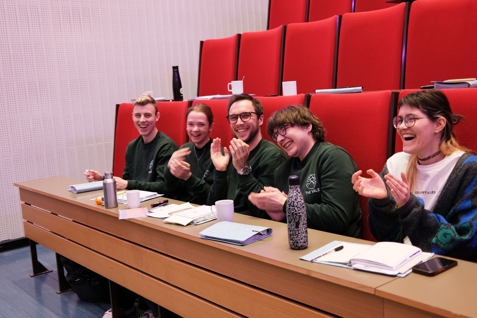 The VALE team applauding and laughing together from red lecture-hall seats